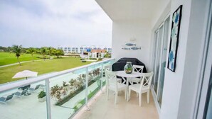 Ein Balkon mit Glasgeländer, weißen Stühlen, einem Tisch mit einer Vase und einem Grill.