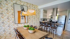 Ein Essbereich mit Holztisch, Stühlen und Blumentöpfen. Im Hintergrund ist eine Küche mit modernen Geräten zu sehen.