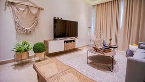Ein modernes Wohnzimmer mit Flachbildfernseher, einer Couch, einem Couchtisch und Zimmerpflanzen.