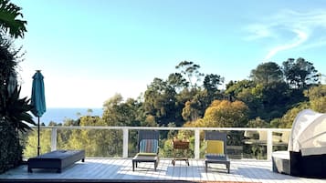 A swimming pool with lounge chairs and a table, surrounded by a deck with a view of trees and the sky.