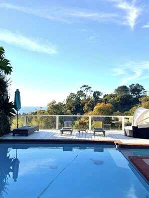 A swimming pool with lounge chairs and a table, surrounded by a deck with a view of trees and the sky. - Ocean Breeze Heaven Pool House in La Jolla (San Diego)