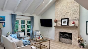 A spacious living room with a high ceiling, a stone fireplace, a television mounted on the wall, and a comfortable seating area with a sofa and armchairs.