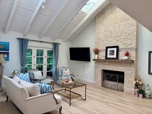 A spacious living room with a high ceiling, a stone fireplace, a television mounted on the wall, and a comfortable seating area with a sofa and armchairs. - Ocean Breeze Heaven Pool House in La Jolla (San Diego)