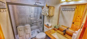 A bathroom with a glass-enclosed shower, a wooden vanity, and a toilet.