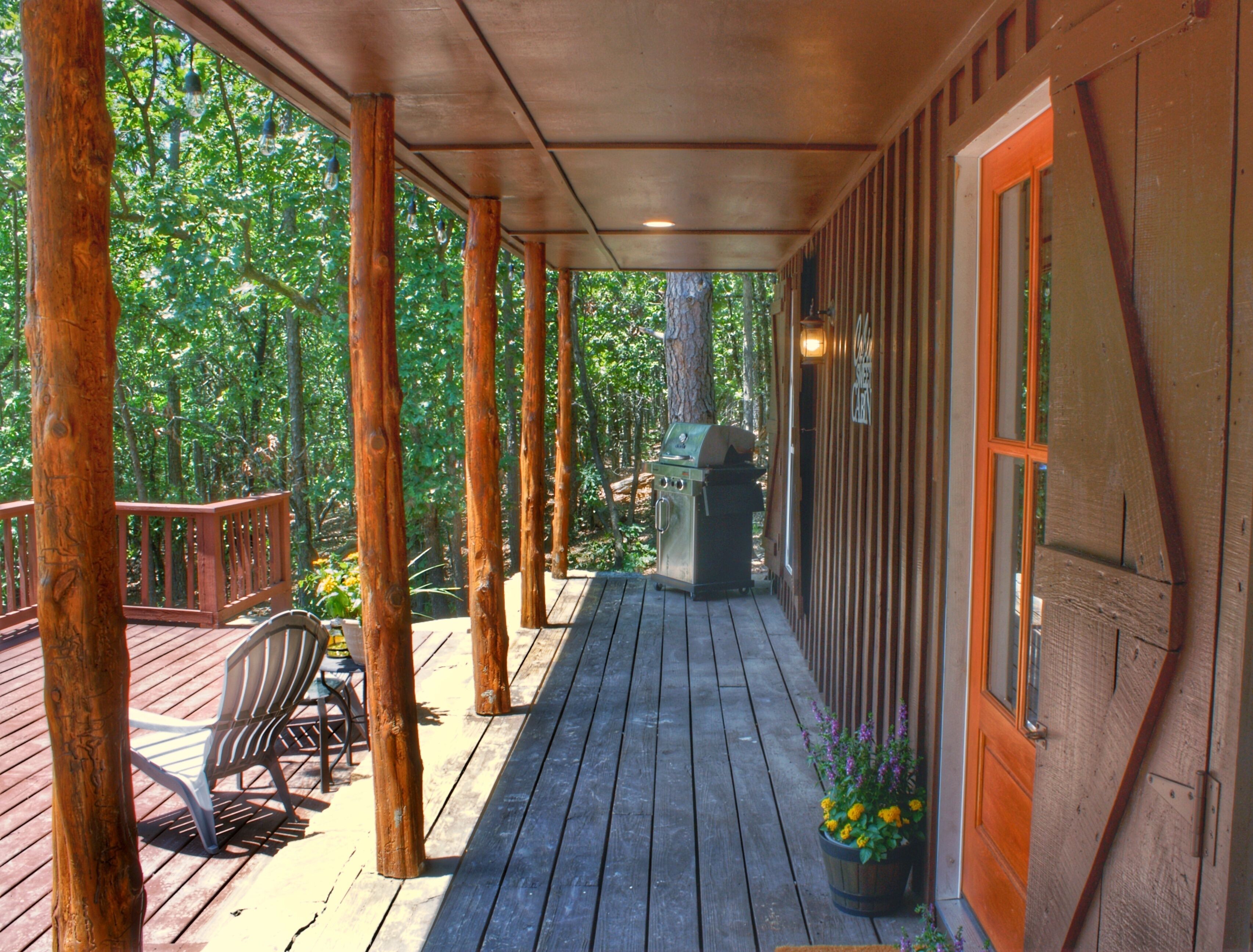 A wooden deck with a grill and potted plants, surrounded by trees.