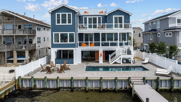 A two-story house with a swimming pool, a deck, and a dock extending into the water. - Beautiful Bayfront w/ Heated Pool & Dock.  6 Bedrooms, all w/ Ensuite Bathrooms. (Ship Bottom)