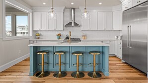 A modern kitchen with white cabinets, a stainless steel refrigerator, and a blue island with four stools. - Beautiful Bayfront w/ Heated Pool & Dock.  6 Bedrooms, all w/ Ensuite Bathrooms. (Ship Bottom)