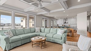 A spacious living room with a large sectional sofa, a round coffee table, and a view of the city through large windows. - Beautiful Bayfront w/ Heated Pool & Dock.  6 Bedrooms, all w/ Ensuite Bathrooms. (Ship Bottom)