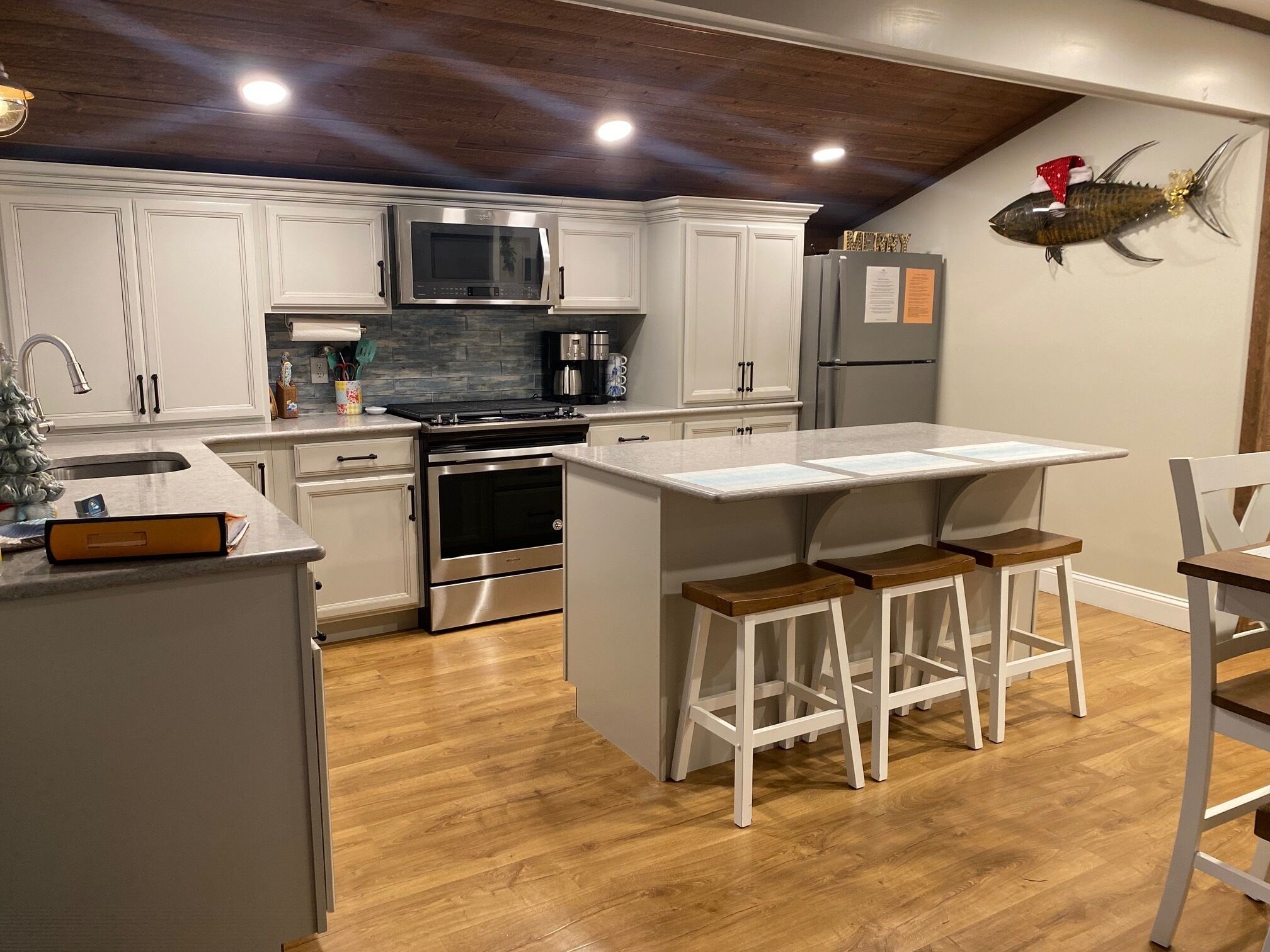 A modern kitchen with white cabinets, stainless steel appliances, a wooden floor, and a fish decoration on the wall.