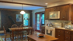 A spacious kitchen with wooden cabinets, a dining table, and a large window. - Bolton Landing - 4 Bdrm Vacation Rental (Bolton Landing)