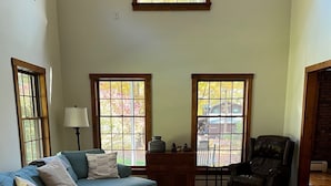 A living room with a sectional sofa, a brown armchair, a glass coffee table, and a fireplace. - Bolton Landing - 4 Bdrm Vacation Rental (Bolton Landing)