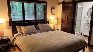 Une chambre à coucher comprenant un lit, deux lampes de chevet, une fenêtre avec des stores, une porte et une petite table de chevet.