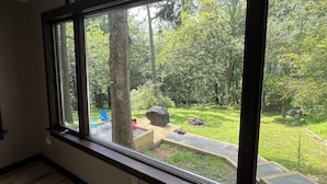 Une pièce dotée d’une grande fenêtre en arc donnant sur un jardin avec une terrasse en bois, un arbre et du mobilier d’extérieur.