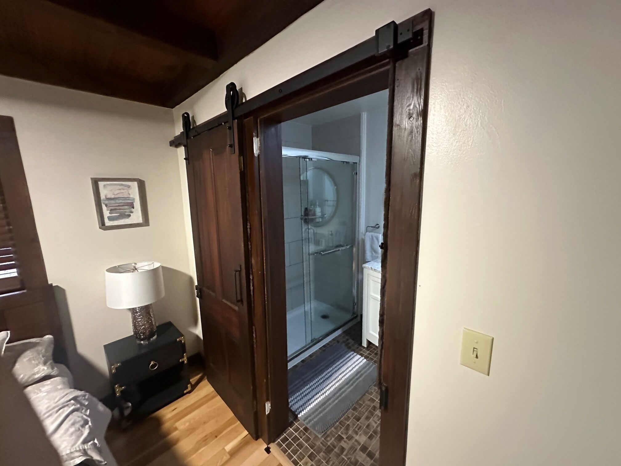 A room with a wooden door leading to a bathroom with a glass shower enclosure.
