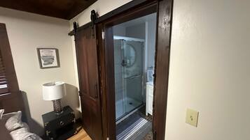 A room with a wooden door leading to a bathroom with a glass shower enclosure.