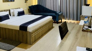 A hotel room with a bed, a desk with a chair, a sofa, a curtain, and an air conditioning unit. - NASHERA HOTELS DODOMA (Dodoma)