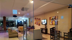 A modern lobby with a glass partition, comfortable seating, a television, and artwork on the walls. - NASHERA HOTELS DODOMA (Dodoma)