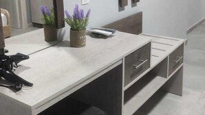 Et moderne, minimalistisk soveværelse med en stor seng, et natbord og et TV ophængt på væggen.