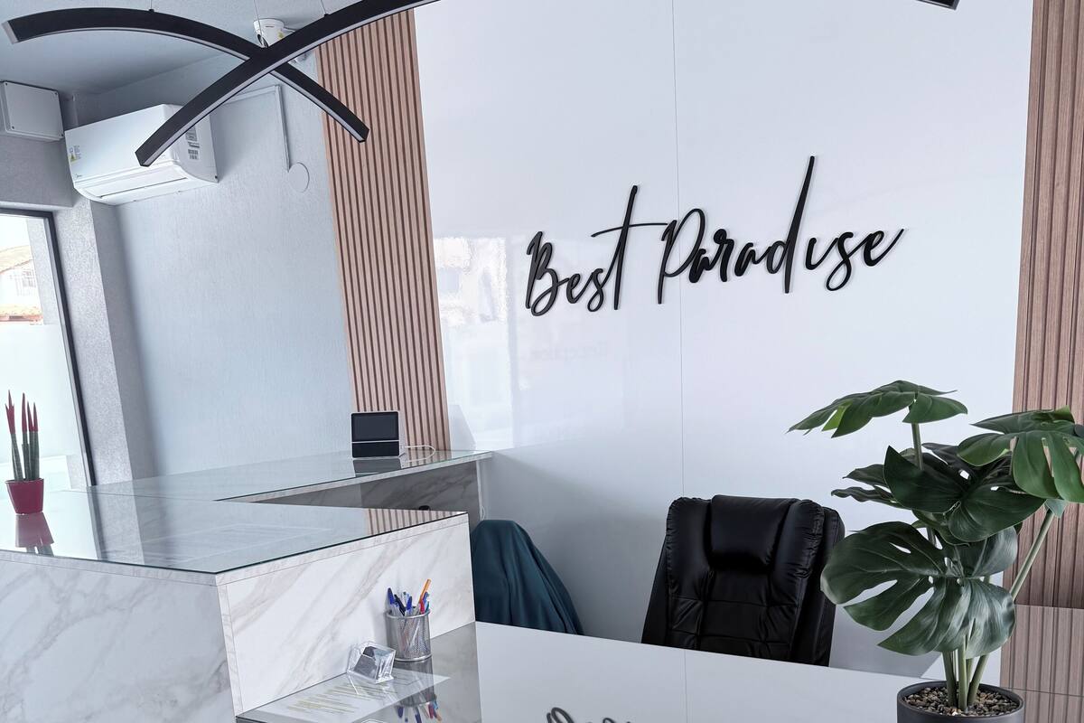 Un mostrador de recepción con encimera de mármol, una planta en maceta y una pared con el texto "Best Paradise".