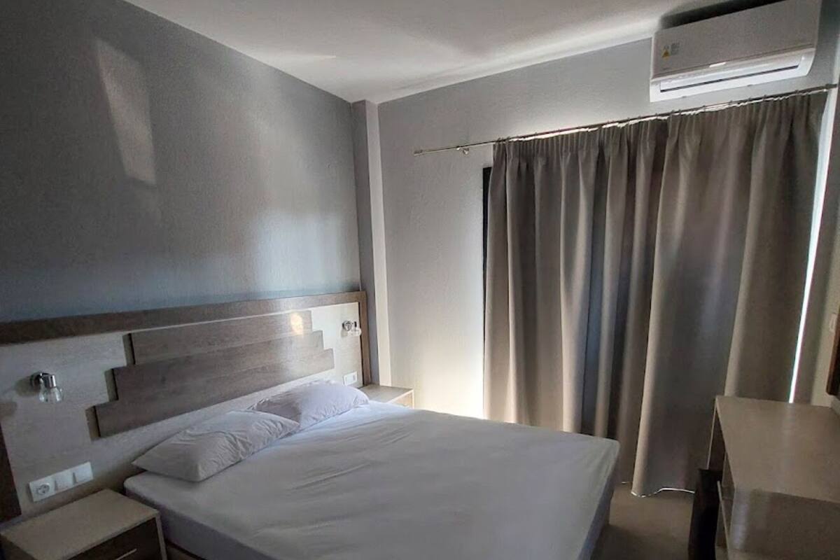 Una habitación de hotel moderna con una cama grande, mesitas de noche, un escritorio y un equipo de aire acondicionado.