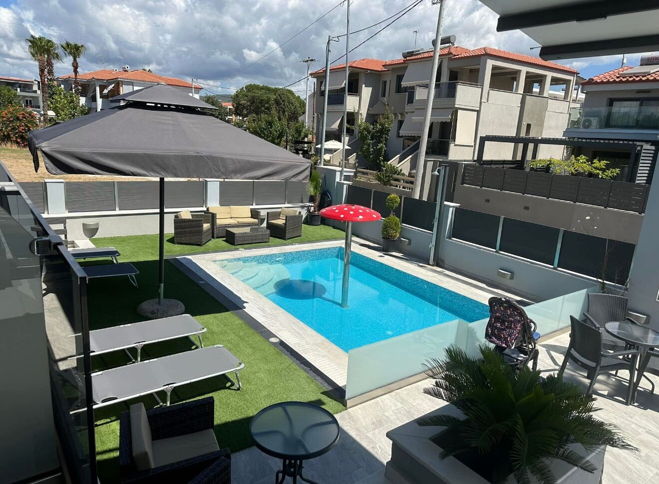 Piscina con sombrilla, mobiliario exterior y vista a edificios cercanos.