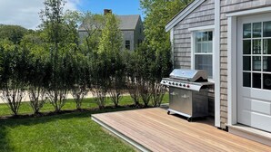 A backyard with a wooden deck, a barbecue grill, and a house with a gray siding exterior. - Charming new construction 4br cottage in town (Nantucket)
