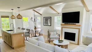 A modern living room with a large sofa, a dining area with chairs and a table, a kitchen with a central island, and a fireplace. - Charming new construction 4br cottage in town (Nantucket)