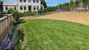 A residential property with a well-maintained lawn, a wooden fence, and a variety of flowering plants. - Charming new construction 4br cottage in town (Nantucket)