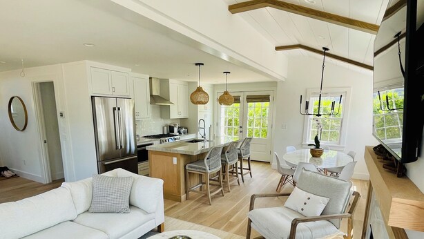 A modern kitchen with white cabinets, a stainless steel refrigerator, and a dining area with a round table and chairs. - Charming new construction 4br cottage in town (Nantucket)