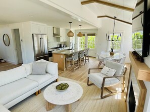 A modern kitchen with white cabinets, a stainless steel refrigerator, and a dining area with a round table and chairs.