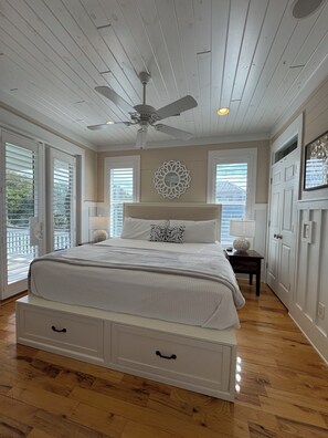 Ein Schlafzimmer mit Bett, Deckenventilator, Holzböden und einem Wanddekor.