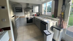 A modern kitchen with white cabinets, a stainless steel oven, a dishwasher, and a large window providing natural light.