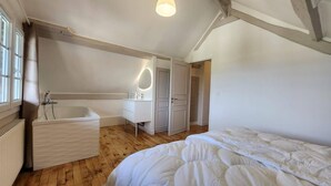 A bedroom with a large bed, a built-in bathtub, and a vanity with a mirror.