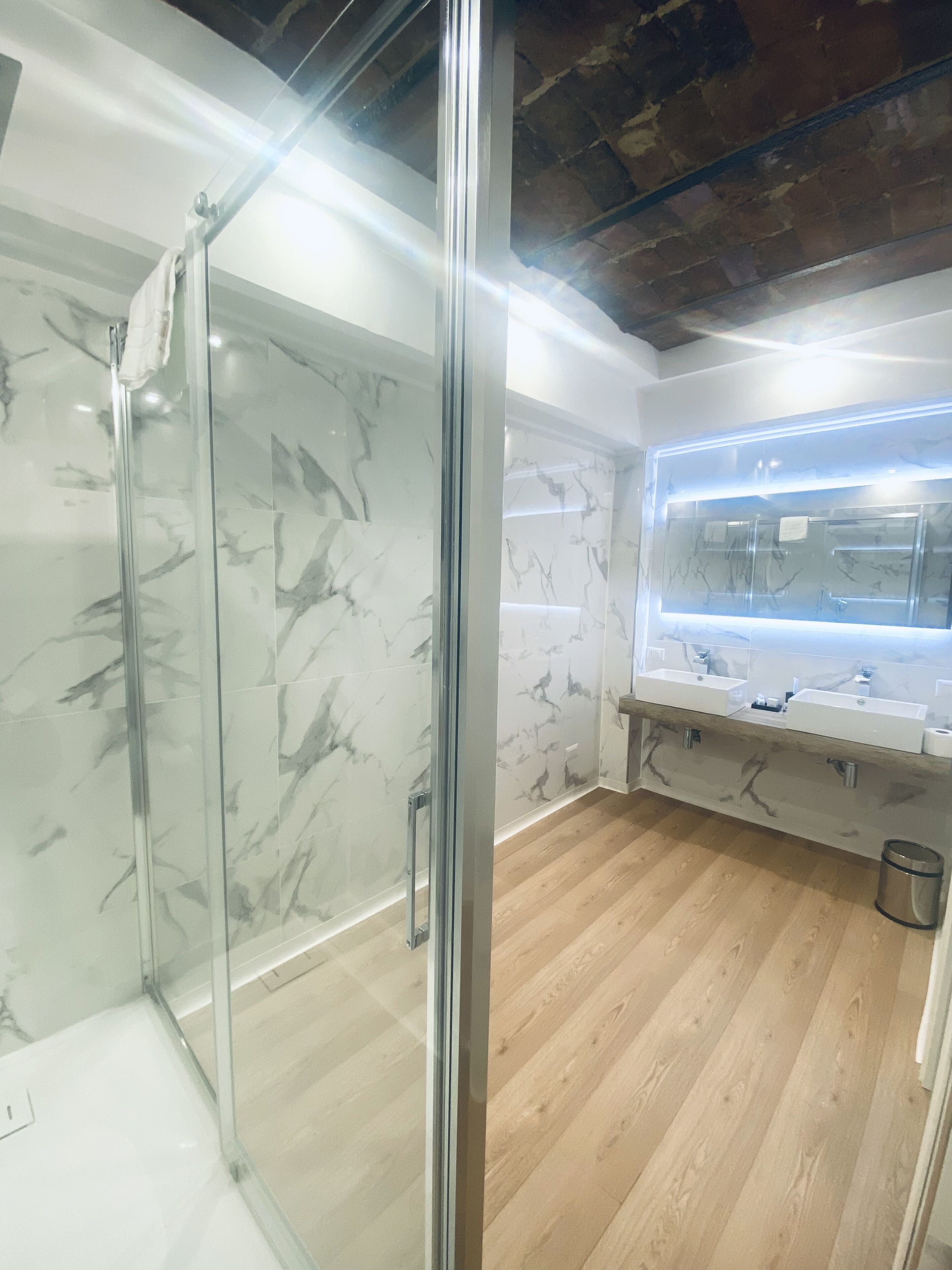 Une salle de bain moderne avec une douche à parois de verre, des murs en marbre et un plancher en bois.