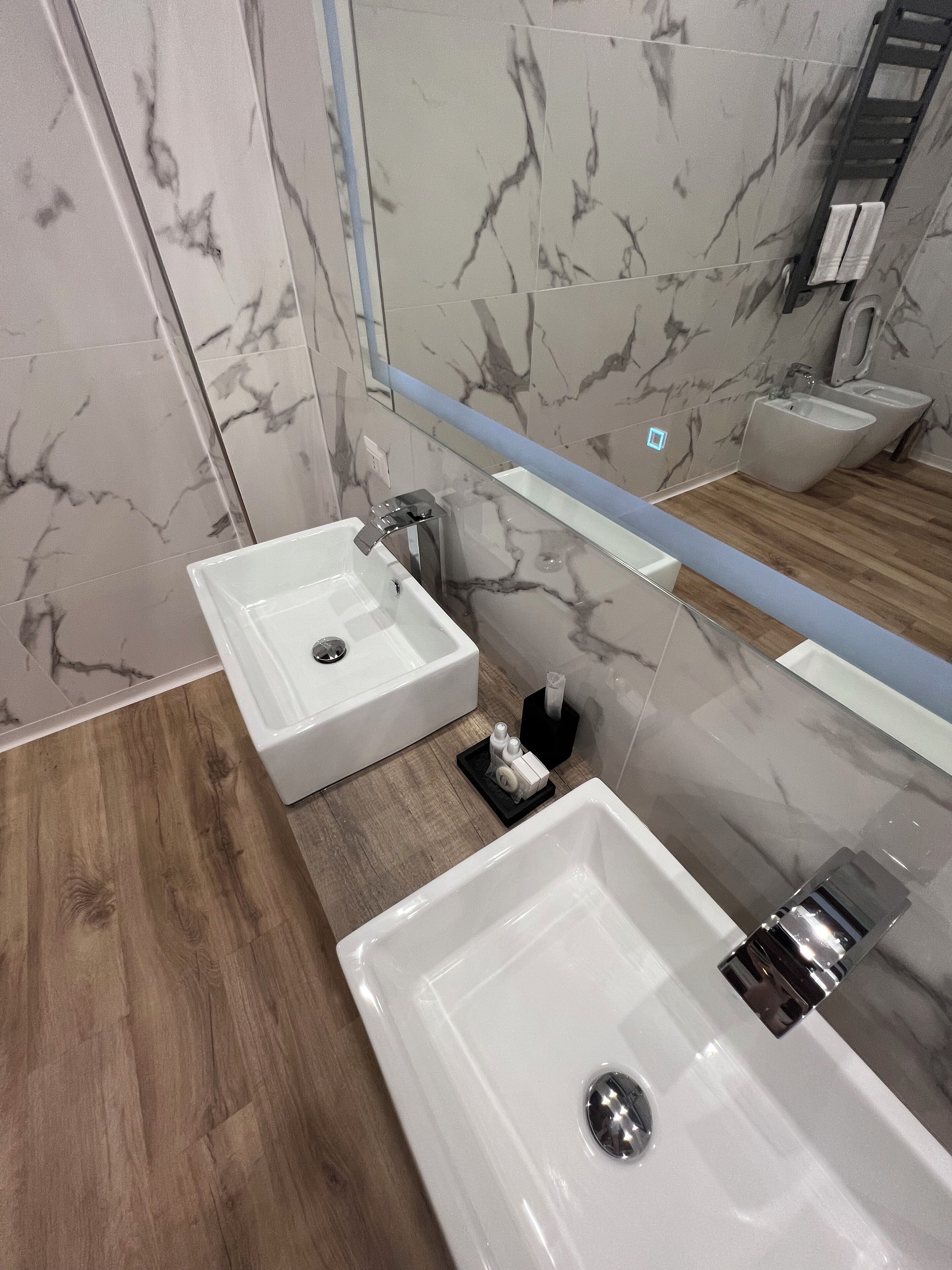 A modern bathroom with two white sinks, a mirror, and a wooden floor.