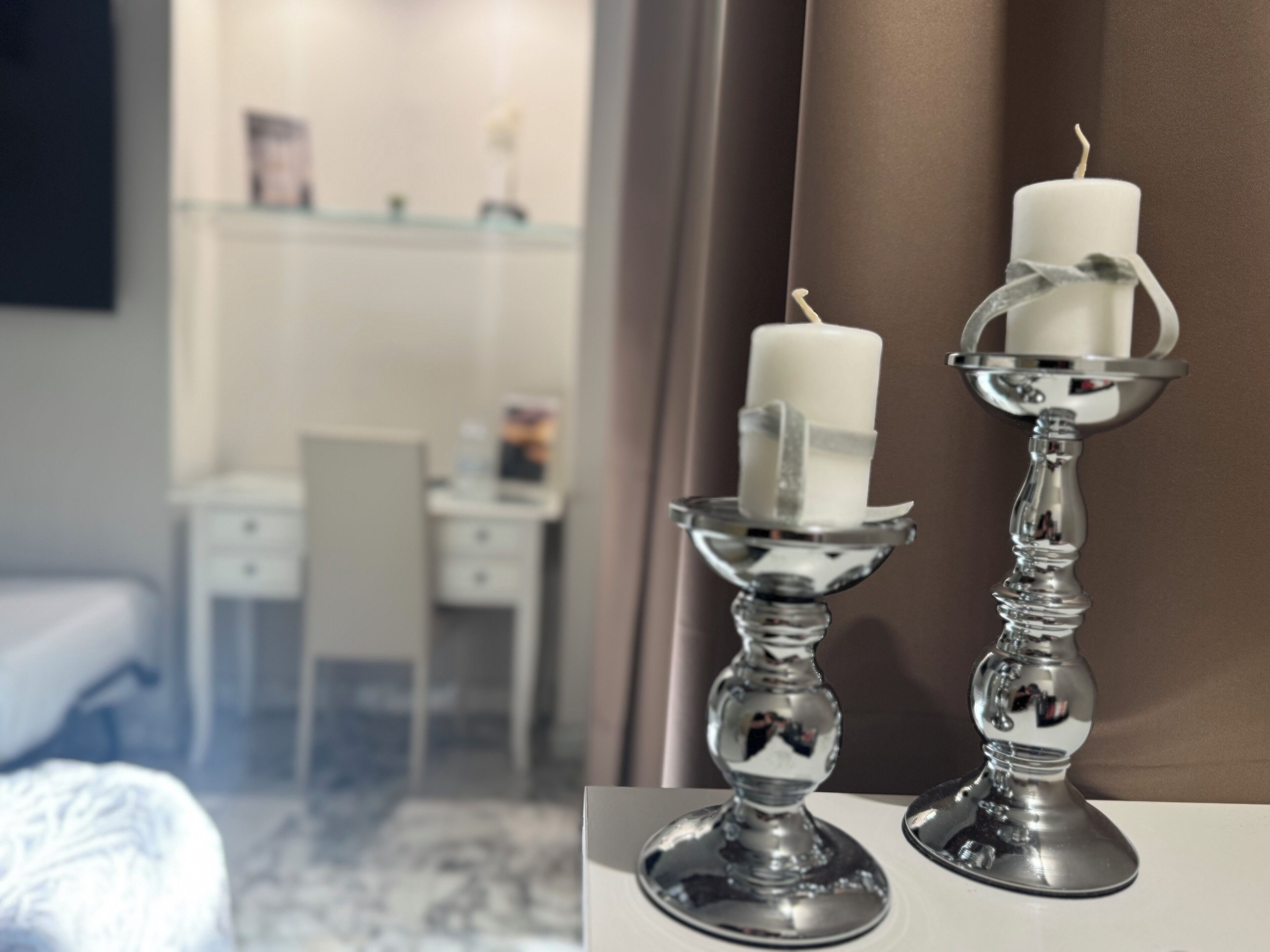 Una habitación de hotel con una cama, un escritorio y dos velas blancas sobre candelabros de plata.