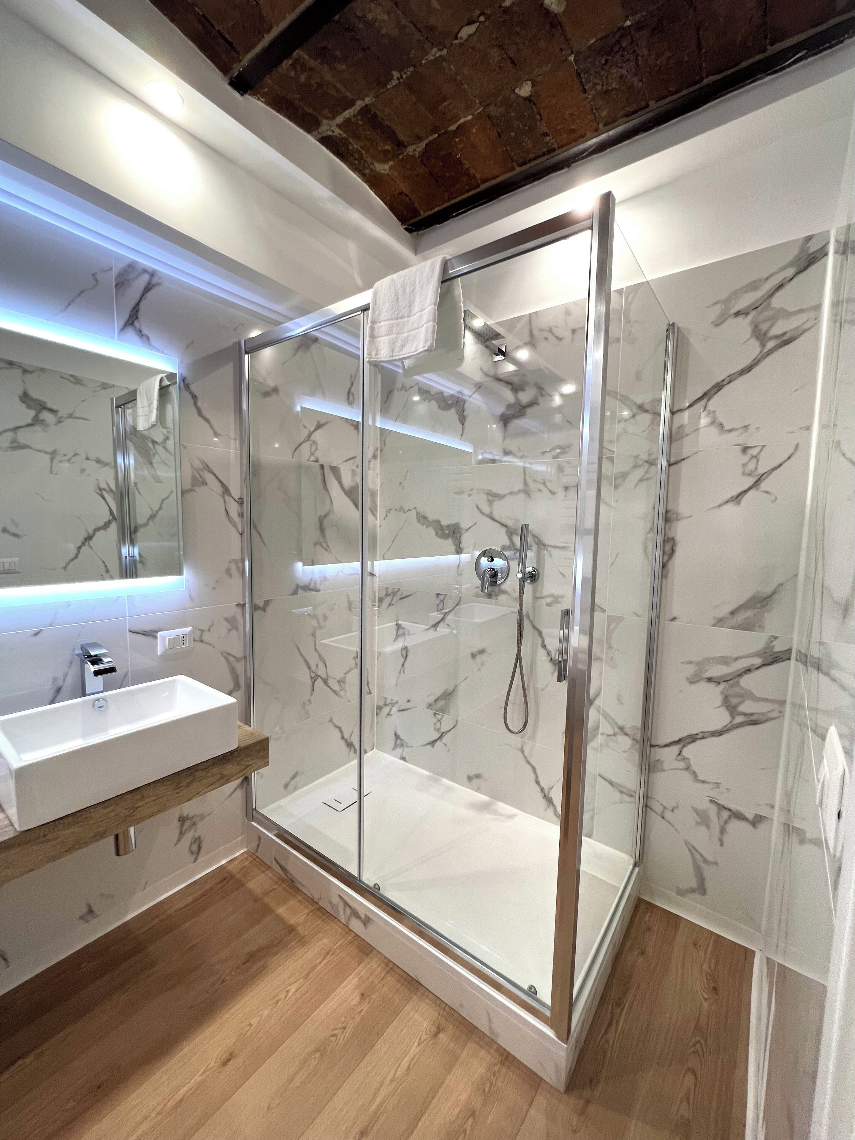 Une salle de bain moderne avec une douche à parois de verre, un mur recouvert de carreaux de marbre et un meuble-lavabo en bois.