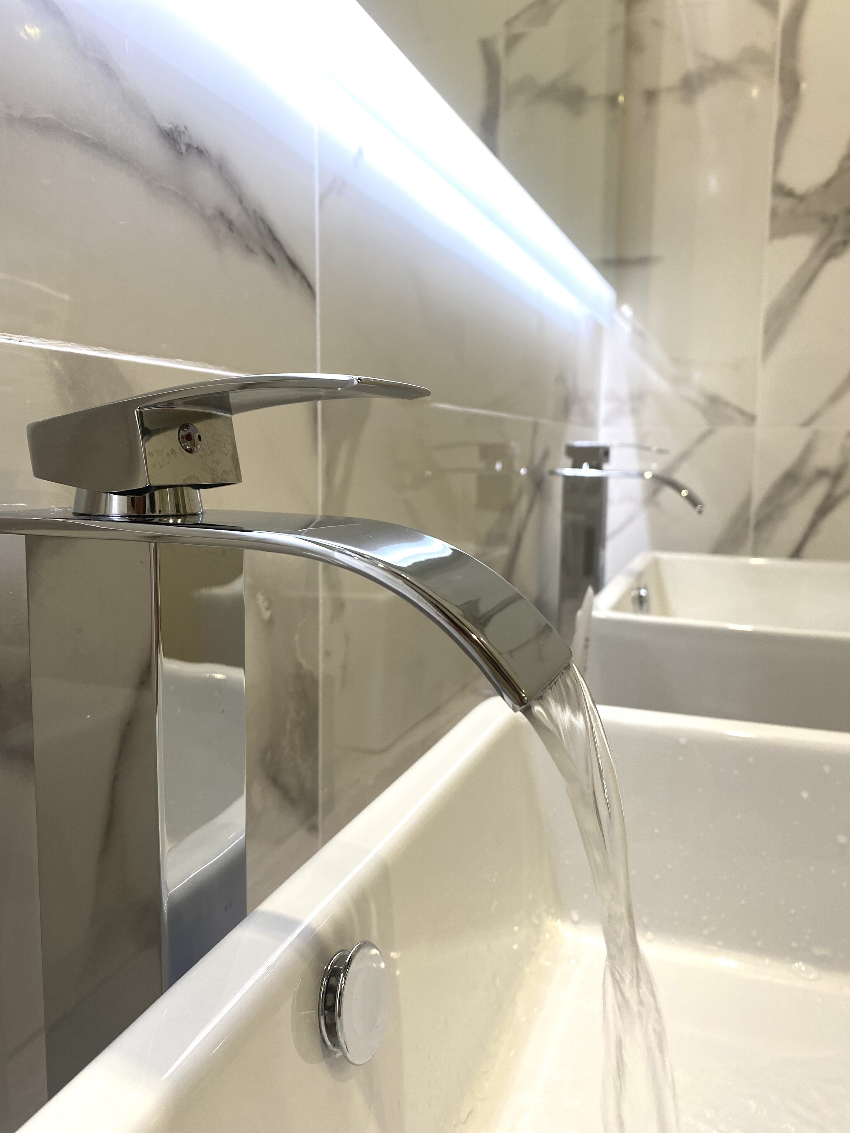 A modern bathroom with a chrome faucet and a marble wall.