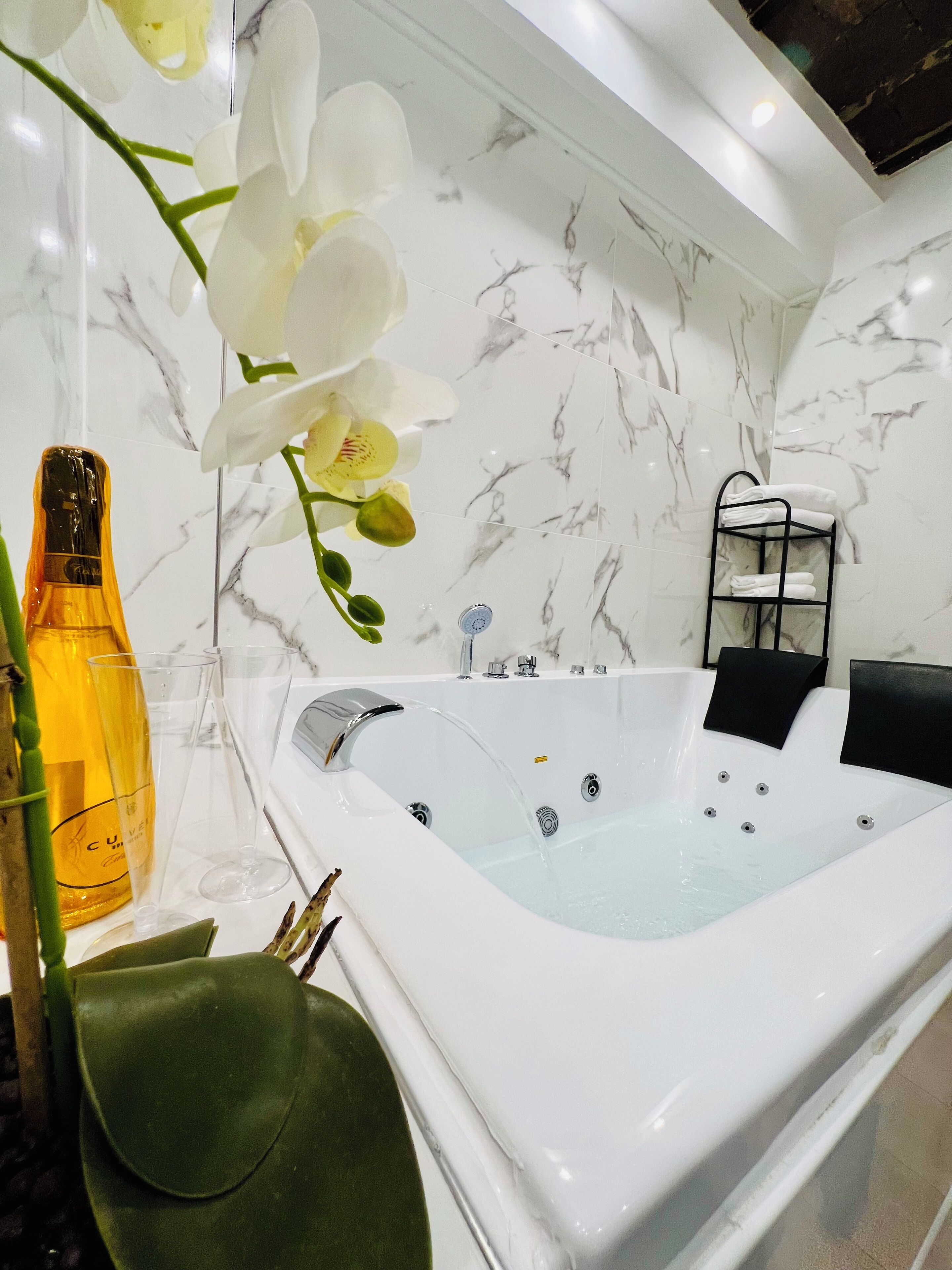 A modern bathroom with a marble wall, a white bathtub, a towel rack, and a green chair.