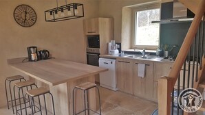 A kitchen with a wooden countertop, bar stools, a coffee maker, a microwave, a dishwasher, and a window providing natural light. - Gîte des Fayettes - Chambost Longessaigne (CHAMBOST LONGESSAIGNE)