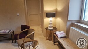 A small, cozy room with a wooden floor, a door, a lamp, a chair, a small table, and a radiator. - Gîte des Fayettes - Chambost Longessaigne (CHAMBOST LONGESSAIGNE)