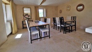 A dining area with a wooden table and chairs, a mirror on the wall, and a window with curtains. - Gîte des Fayettes - Chambost Longessaigne (CHAMBOST LONGESSAIGNE)