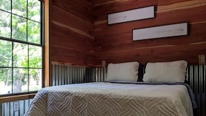 Una habitación con paneles de madera, una cama, dos letreros en la pared y una ventana con vistas a árboles.
