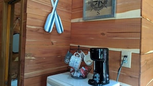 Interior de una cabaña de madera con una cafetera, tazas y una brújula en la pared.