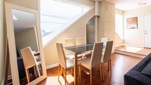 A dining area with a glass table and chairs, a view through a window, and a brick wall. - Modern Apt above Restaurant. Walkable Shops & Bars (Louisville)