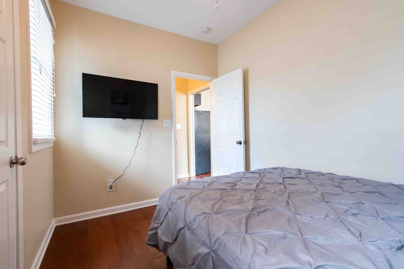 A bedroom with a bed, a wall-mounted TV, and a door leading to another room.