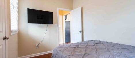 A bedroom with a bed, a wall-mounted TV, and a door leading to another room.