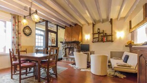 A cozy living room with a wooden dining table, chairs, a fireplace, a sofa, and a television.