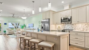 A modern kitchen with a large island, bar stools, a refrigerator, microwave, and a tiled backsplash. - Scenic Sandpiper by the Shore (Long Beach)