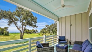 A covered outdoor area with wicker furniture, a white railing, and a view of the ocean. - Scenic Sandpiper by the Shore (Long Beach)